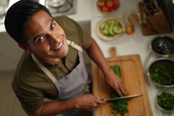 Man preparing a fresh herb salad in kitchen, smiling while making dinner
