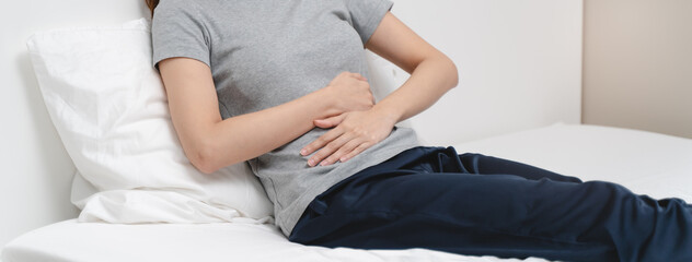 Menstruation symptom concept, Close-up woman touching her belly and feeling stomach pain from cycle period on the bed at home.