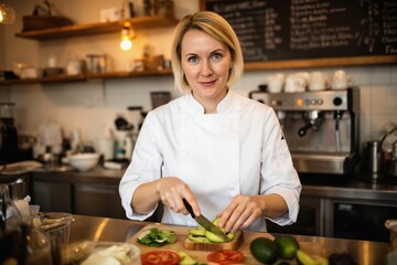 Friendly blonde chef preparing avocado and salad in a modern cafe kitchen