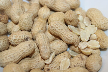 Peanuts in their shells and raw nuts arranged on a white plate for a snack or recipe preparation