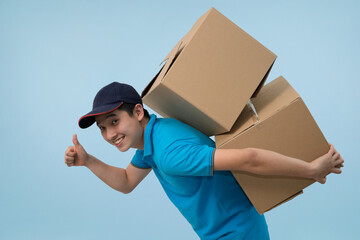 Happy young Asian male courier smiling confidently while carrying two large cardboard delivery boxes and giving a thumbs up, symbolizing approval, excellent service, and reliability