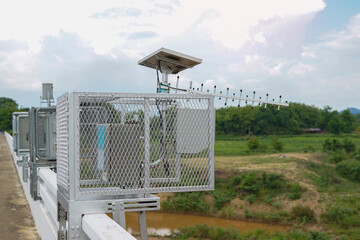 A metal cage housing a remote water level sensor and an antenna, powered by a small solar panel, installed next to a river to monitor water levels and provide flood warnings.