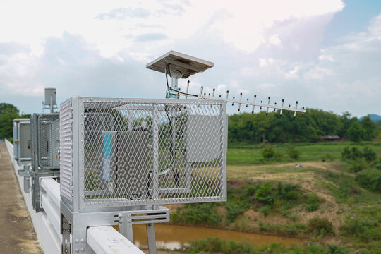 A metal cage housing a remote water level sensor and an antenna, powered by a small solar panel, installed next to a river to monitor water levels and provide flood warnings.