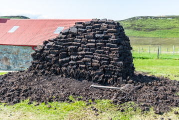 A stack of peat is stored for the winter beside a rural house in northern Scotland. Pile of peat.