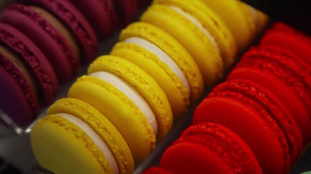 Vibrant close-up of assorted macarons displayed in neat rows showcasing vivid yellow, red, and purple shells with delicate textures and creamy fillings in shallow depth of field.