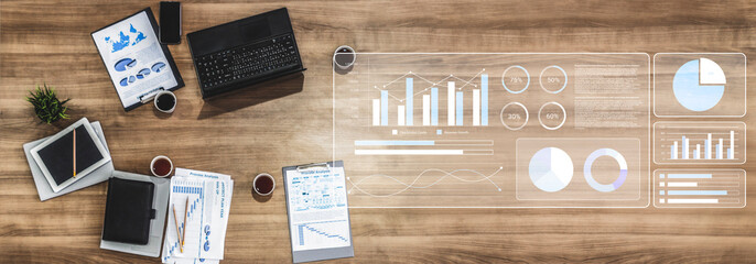 Modern workspace featuring digital analytics and charts on a wooden desk, with a laptop, paperwork, and coffee, ideal for business planning and analysis. Gantry