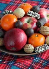 festive plate with apples and tangerines, chocolates and walnuts on a checkered tablecloth