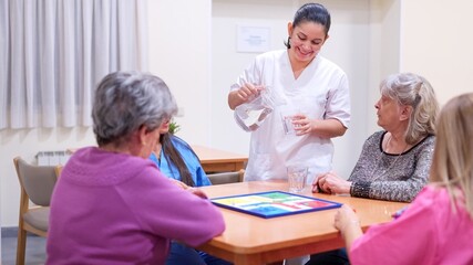 Obraz premium Caregiver serving water to senior women playing board game