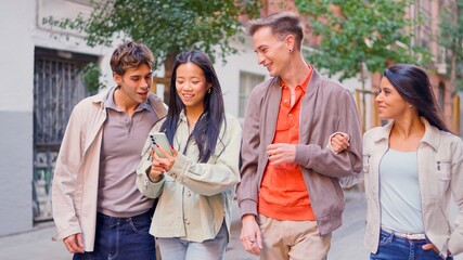 Diverse group of friends walking city street watching smartphone