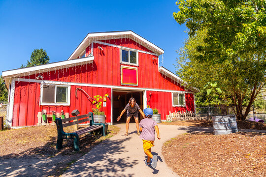 Child running towards mother in front of red barn at the bc wildlife park in kamloops