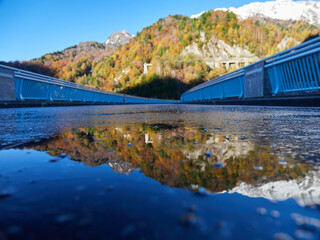 秋の観光名所立山黒部アルペンルートの黒部ダムの貯め水に映すカラフルな紅葉と初雪の雪山の風景