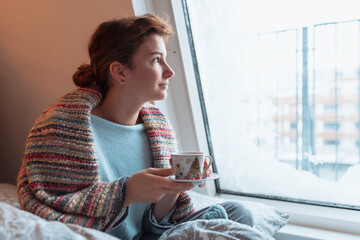 young woman warms up with hot tea in winter weather at home