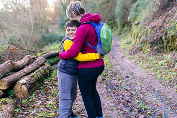 Mother embracing her son with down syndrome on a forest trail, showing love and connection during outdoor activity