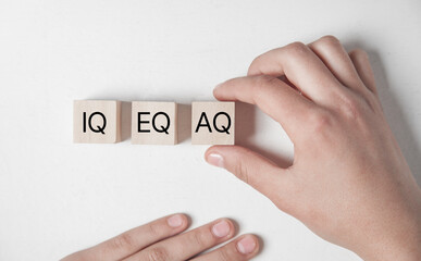 Wooden blocks with the letters IQ, EQ and AQ representing Intelligence Quotient, Emotional Quotient, Adaptability Quotient. A hand adjusting AQ block, symbolizing adaptability in modern intelligence.