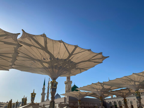 Low-angle view of the majestic retractable umbrellas providing shade in the courtyard of Al Masjid an Nabawi in Medina. The umbrellas feature intricate geometric patterns and golden columns.