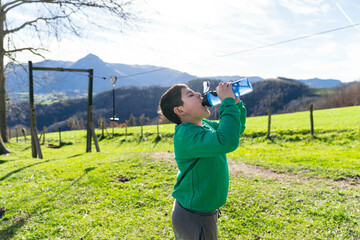 Boy drinking water from a plastic bottle, staying hydrated during outdoor activity in a green field...
