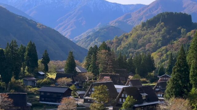 Upward pan moves from the rice fields to Ainokura village in Toyama, Japan, before revealing the forested hills and distant snowy peaks of the Japanese Alps