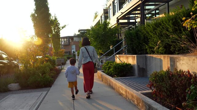 Warm sunset lighting illuminating mother and son walking hand in hand along quiet residential street, sharing peaceful moment of connection and love in vancouver neighborhood