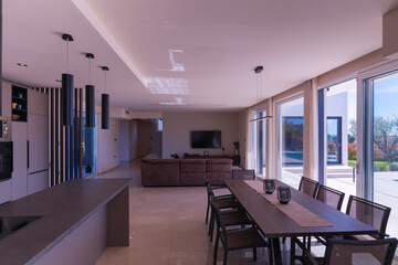  Modern open-plan living and dining room in a luxury villa with large glass doors opening to a private swimming pool, offering a spacious and elegant indoor-outdoor living experience