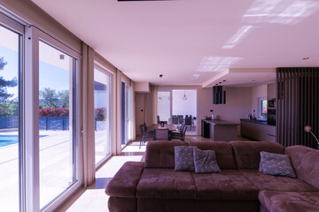  Modern open-plan living and dining room in a luxury villa with large glass doors opening to a private swimming pool, offering a spacious and elegant indoor-outdoor living experience