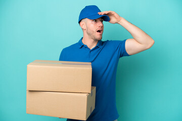 Delivery caucasian man isolated on blue background doing surprise gesture while looking to the side
