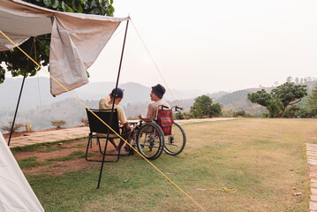 Two friends relax at a campsite on a mountain viewpoint, sharing conversation and enjoying nature together. A wheelchair user and companion experience friendship, inclusion, peaceful outdoor travel.
