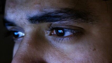 close up detail of focused male eyes staring at computer monitor screen with blue light reflection in dark night © Sabbir