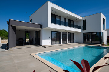 Modern luxury villa with swimming pool and clean minimalist architecture under a blue sky. Contemporary residential exterior featuring large windows, terrace, and elegant outdoor living space