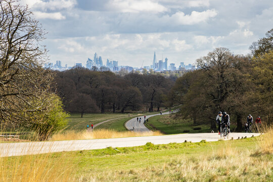 Cyclists riding uphill through a London park with city skyline in the distance