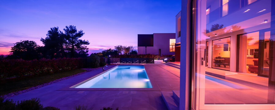 Modern luxury villa with a luminous swimming pool at twilight. Contemporary architecture, sleek design, and inviting interior lights create a serene and elegant evening ambiance, ideal for upscale
