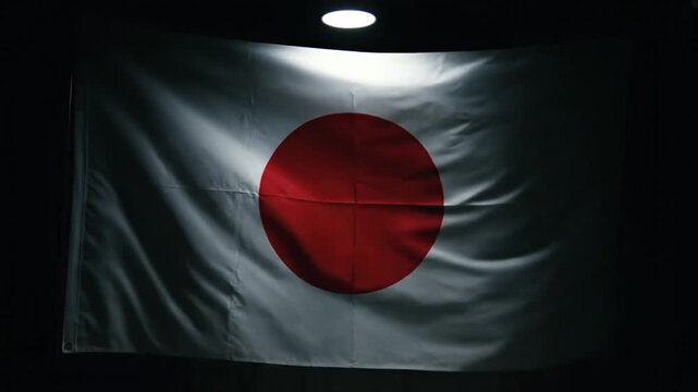 A white flag featuring a large red circle in the center illuminated from above by a bright light in a dark setting