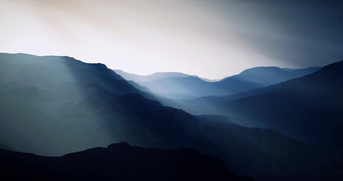 Fog envelops the mountain ranges as soft light filters through during twilight. The peaks appear silhouetted against the serene horizon, creating a peaceful and atmospheric landscape.