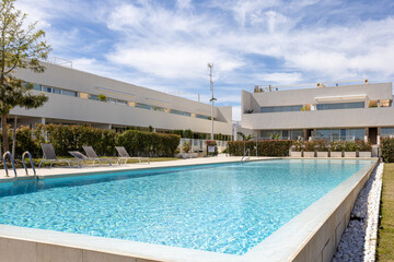 Modern residential complex with outdoor swimming pool and sun loungers on a sunny day
