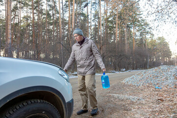 man outside the city standing by his car with a bottle of washer fluid. Car maintenance on the road concept.
