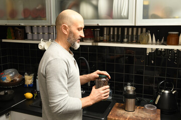 Man prepares coffee in modern kitchen while holding a jar of coffee beans during morning routine