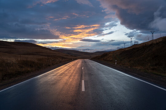 Wet Highway at Dusk Reflecting Orange Sunset Light Under Overcast Sky.