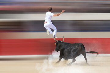 Athlete jumping over charging black bull in arena with motion blur background action shot