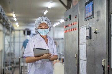 Female inspector wearing protective gear and hairnet examines canned fish production quality, checks Industrial pressure cooker, monitors food processing , and records data using tablet.