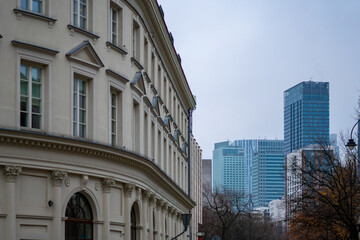 Historic townhouse facade with columns in foreground contrasted by modern Warsaw skyscrapers under overcast urban sky