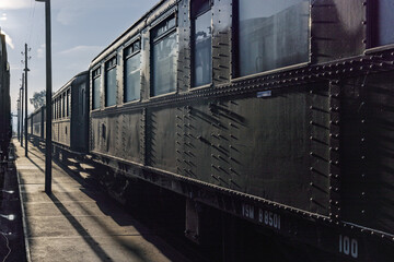 Perspective view of vintage dark green riveted passenger train carriages parked at the platform during a sunny day at the railway museum.