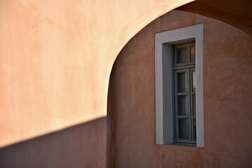 Fototapeta premium Adobe house grey wooden window with a white trim on a light peach Venetian stucco wall in Oia Santorini island, Cyclades Greece.