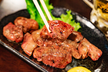 箸で持ち上げられた照り焼き風の濃厚な鶏レバー（レバー焼き