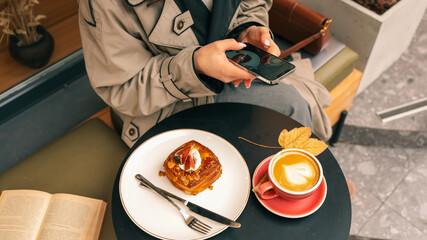 Woman using smartphone at cafe table with pastry and latte art coffee