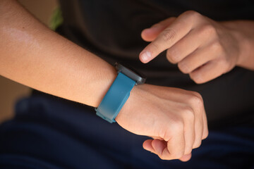Young individual wearing a blue smartwatch is interacting with the device on their wrist, showcasing modern technology and personal fitness tracking in a casual setting