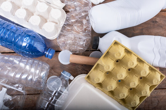 Various types of plastic and cardboard waste materials scattered on wooden surface, showcasing the importance of recycling and environmental awareness in waste management practices