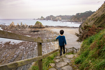 Boy exploring rocky coastline path leading to beach