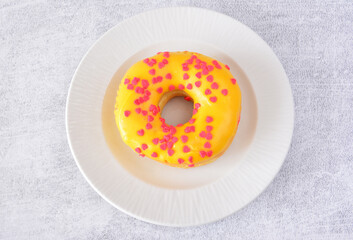 a top view of Yellow Donut with Pink Heart Sprinkles on a White Plate 