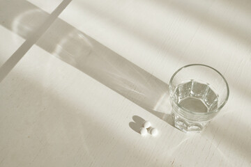 Pills and glass of water on table in natural morning light