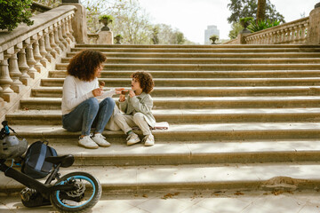 Son and his mother talking and holding ice cream while sitting on a blanket on the stairs