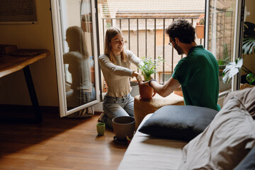 Woman and man holding hands in a potted plant and sitting on the floor while she smiles